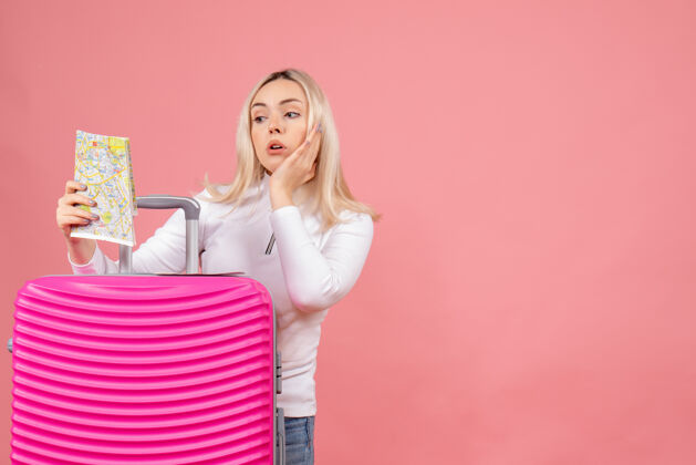 快乐前视图：年轻女士站在粉色手提箱后面看地图站在前面女士成人
