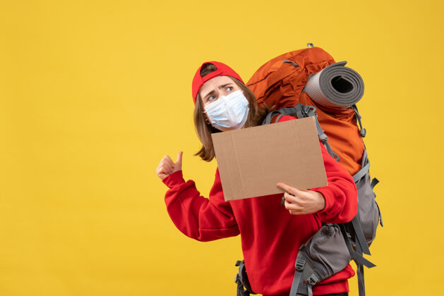 指着正面图年轻的旅行女孩背着背包和面具拿着纸板指着后面面具衣服前面