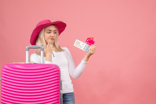 风景正面图年轻女士站在粉红色的手提箱后面 看着卡片和票成人前面手提箱