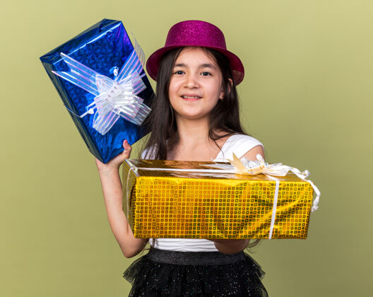 帽子年轻的白人女孩戴着紫色的派对礼帽 手拿礼品盒 橄榄绿的墙上有一个单独的复制空间孤立年轻橄榄