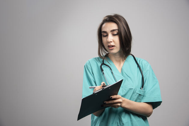 职业女医生在灰色背景上展示笔记高质量照片制服工作工作