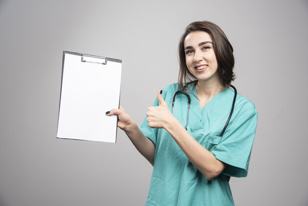 医疗女医生在灰色背景上展示剪贴板高质量照片制服个人医生