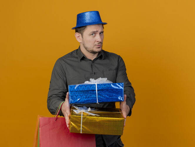 蓝色给人印象深刻的年轻人戴着蓝色的帽子拿着礼品袋盒子孤立在橙色穿着帽子橙色