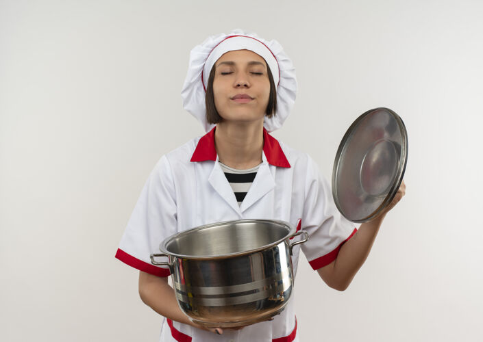 脸高兴的年轻女厨师在厨师制服打开锅盖闭上眼睛隔离在白色的墙壁上制服年轻女