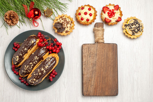 玩具俯瞰图：灰色盘子上的巧克力蛋糕和葡萄干馅饼一块砧板 白色木质地面上放着松树叶子和圣诞玩具木板头发滑松树