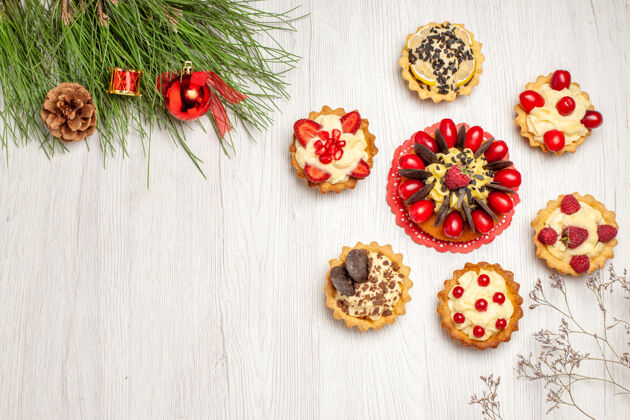蛋挞顶视图浆果蛋糕圆形馅饼和松树叶子与圣诞玩具在白色的木制地面节肢动物松树木头