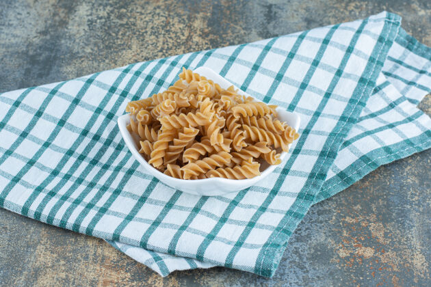 好吃的一碗棕色的意大利面 放在毛巾上 大理石背景上福西利碗美味