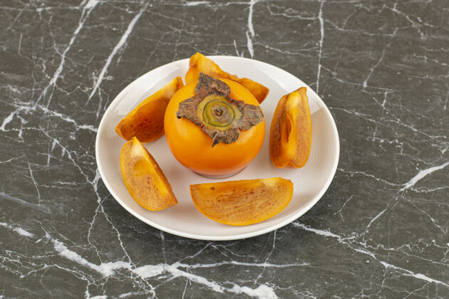 有机新鲜柿子的特写照片整个或切片在白色盘子上秋季热带饮食