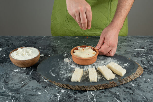 生的男性用手在大理石桌上的面团里加盐糕点准备配料