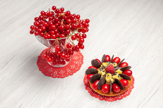 木头在白色木桌上的红色椭圆形蕾丝小桌布上 可以俯瞰水晶玻璃里的红醋栗和浆果蛋糕水晶玻璃花边