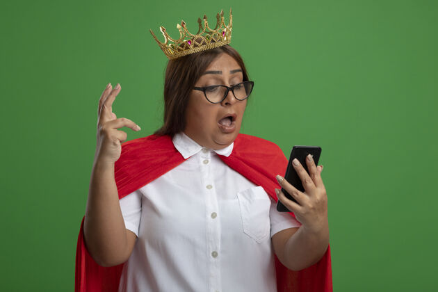 电话惊讶的中年女超人戴着皇冠 举着眼镜 看着绿色的手机绿色超级英雄中年