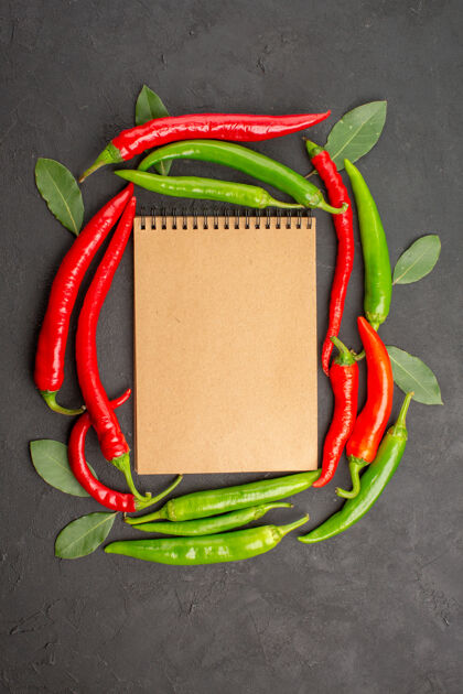 辣椒顶视图一个笔记本在红绿的辣椒圈和黑色背景上的叶子上背包袋子蔬菜