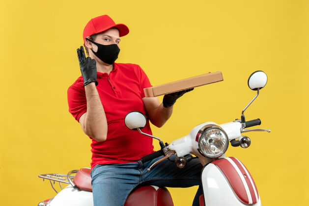 车辆俯视图：一个自信而满意的快递员 穿着红色上衣 戴着帽子手套 戴着医用面罩 坐在滑板车上 显示两个等待命令命令医疗摩托车