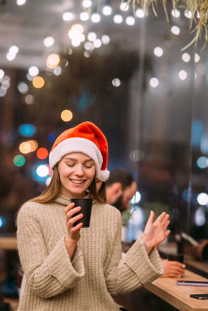 咖啡馆戴着圣诞老人帽子的女孩坐在咖啡店里喝咖啡桌子休闲庆祝