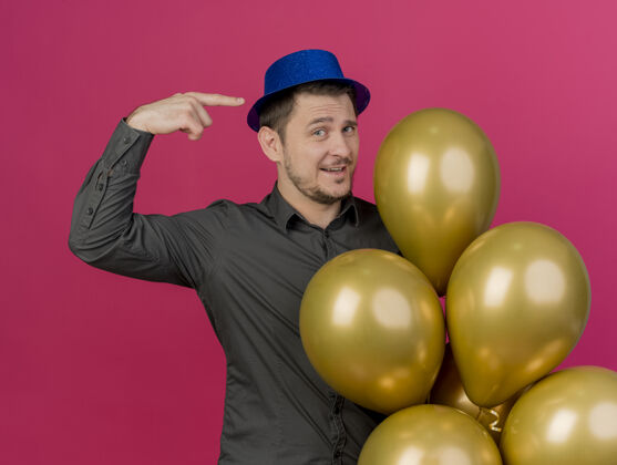 自己高兴的年轻人戴着蓝色帽子拿着气球 指着自己孤立的粉红色请穿年轻