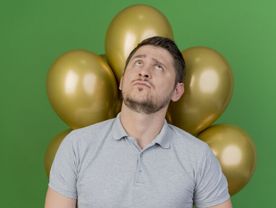 派对看着一个穿着灰色衬衫 体贴的年轻人站在绿色的气球前站着灰色绿色