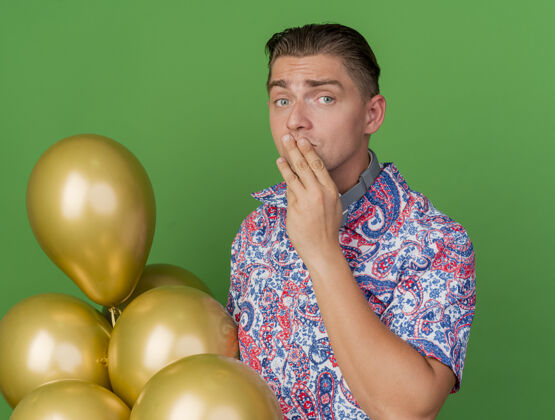 年轻关心党的年轻人穿着五颜六色的衬衫站在旁边的气球把手放在嘴上孤立的绿色站嘴巴气球