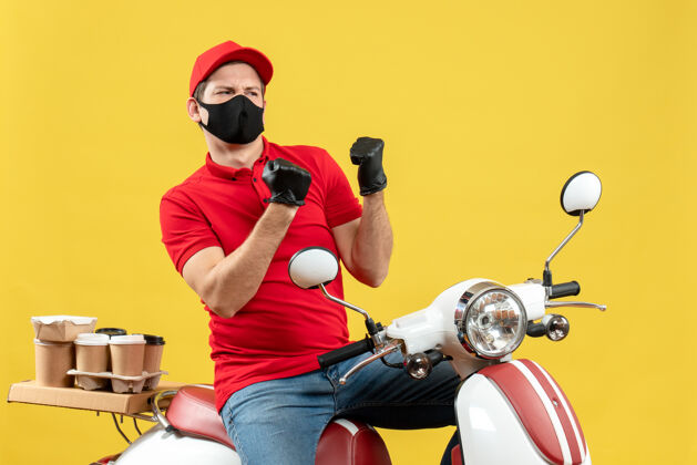 坐俯视图：情绪激动的年轻人穿着红色上衣 戴着帽子 戴着手套 戴着医用面罩 坐在滑板车上发火感情摩托车年轻人