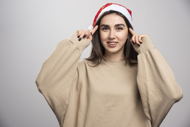 年轻戴着圣诞老人帽子的年轻女子在摄影棚拍摄了一张灰色的照片快乐圣诞老人模特
