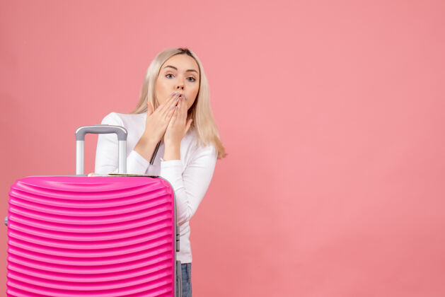 时尚正面图：站在粉色手提箱后面的年轻女士大吃一惊展台手提箱正面