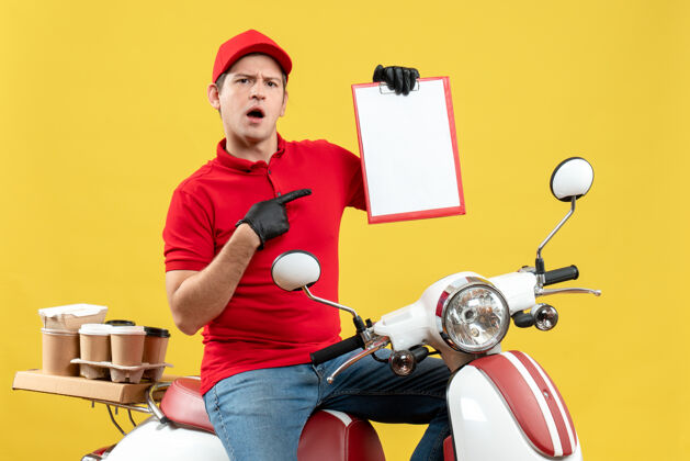 人前视图惊讶的快递员身穿红色上衣 戴着帽子手套 戴着医用口罩 坐在摩托车上拿着文件传递订单车辆摩托车文件