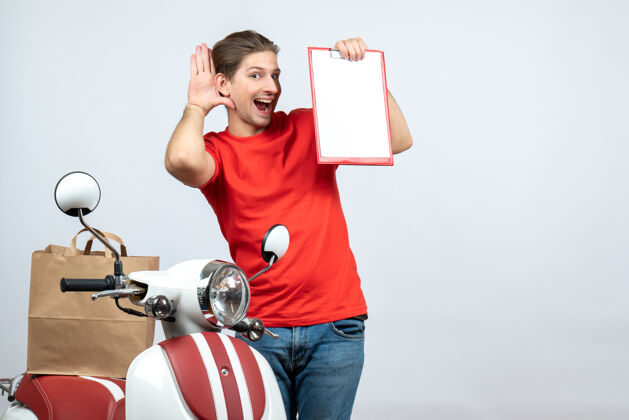 八卦正面图是微笑的送货员 身穿红色制服 站在滑板车旁 展示文件 在白色背景上聆听最后的闲话送货员锻炼文件