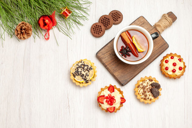 排骨俯视图：一杯柠檬肉桂茶放在砧板上 馅饼 饼干 松树叶子和圣诞玩具放在白色的木头地上叶子松树香料