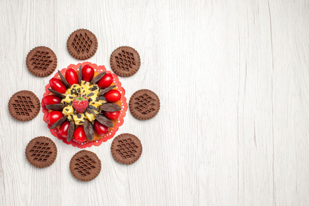 花边左上角是红色椭圆形蕾丝doily上的浆果蛋糕和白色木桌上的饼干木头食物饼干