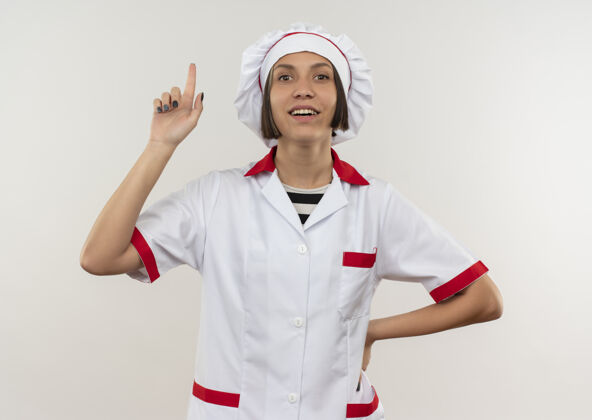 衣服身着厨师制服的年轻女厨师面带微笑 手放在腰上 手指孤立地竖立在白墙上人公民感情