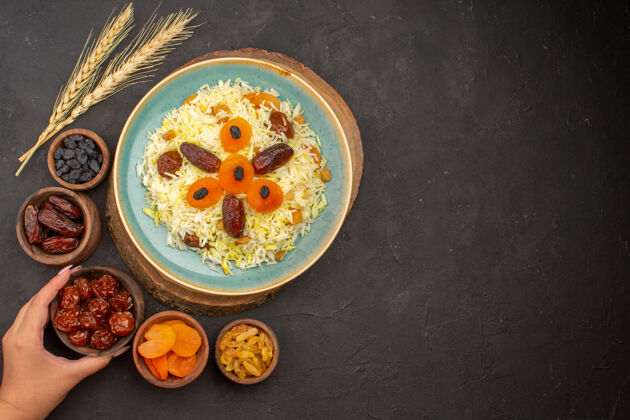 大米美味煮熟的普洛夫米饭的顶视图 在黑暗的表面上 盘子里有不同的葡萄干食物可食用水果深色