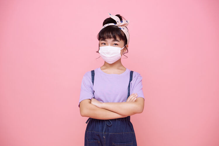快乐亚洲小女孩戴着口罩保护她免受病毒covid-19隔离在粉红色墙上疾病年轻流感