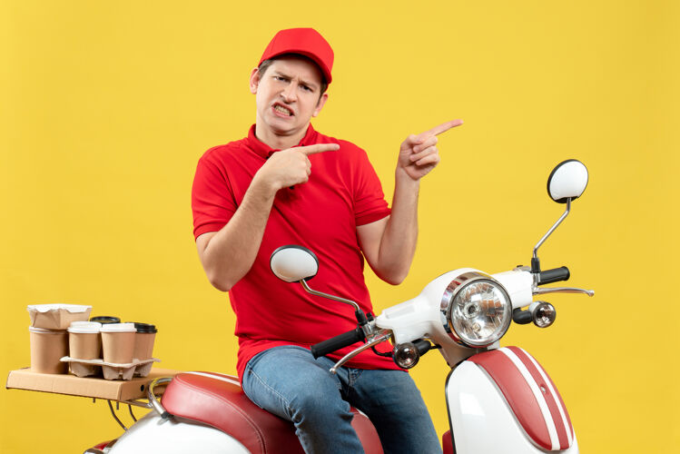 快乐顶视图是一个不满意的年轻人 穿着红色上衣 戴着帽子 指着黄色的墙上的东西发命令传送带摩托车帽子