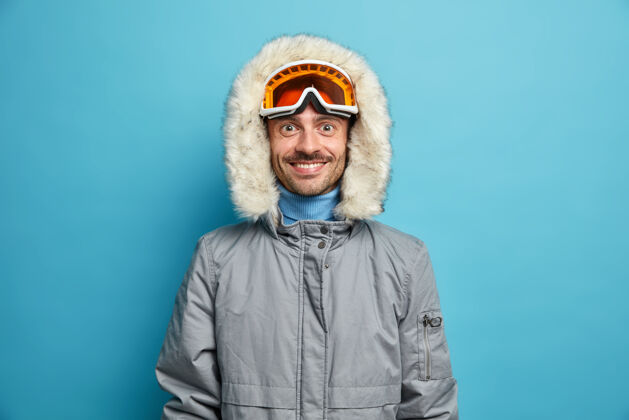 夹克运动型的快乐男人喜欢冬季运动娱乐微笑愉快地戴着滑雪镜和灰色夹克胡茬微笑假期