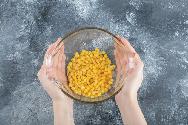 有机女人的手拿着一碗装在大理石上的玉米罐头圆形蔬菜顶视图