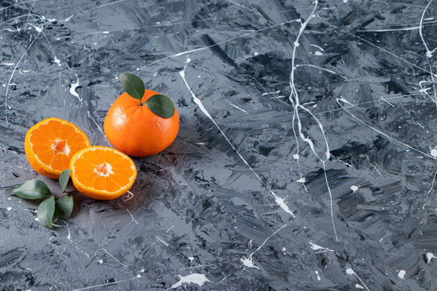 食物整个和切片新鲜的橙色水果与叶子放在大理石表面自然果汁美味