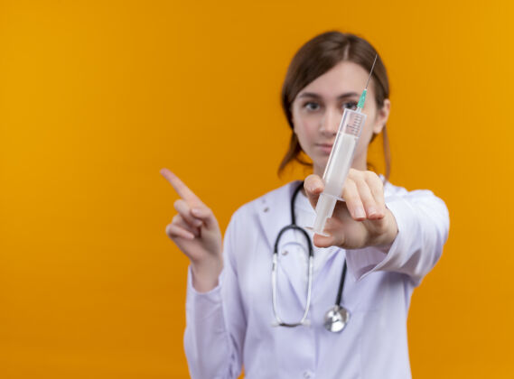 注射器一位面容严肃的年轻女医生 穿着医用长袍 手持注射器 手持听诊器 指着左边的橙色空白处 还有复印空间听诊器复制太空