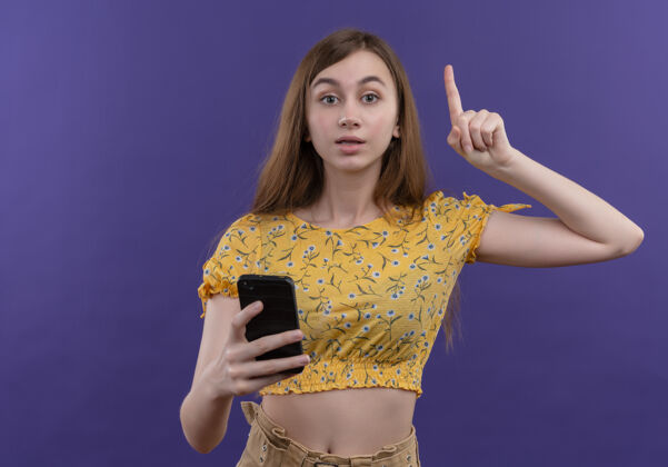 空间印象深刻的年轻女孩有新的想法 拿着手机和提高手指在孤立的紫色空间与复制空间女孩印象紫色