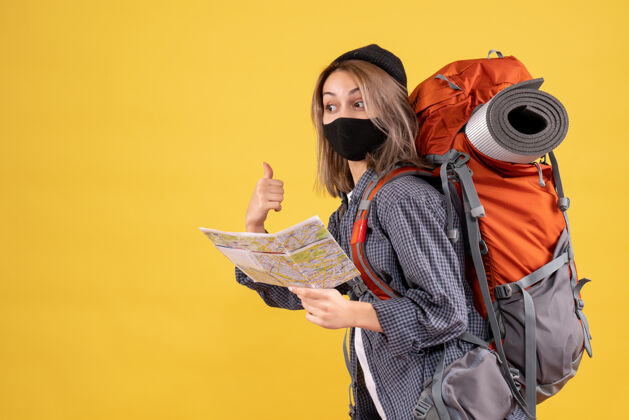 背包可爱的旅行女孩与黑色面具和背包的正面视图举行地图指向后面男性持有指向