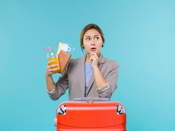 女人前景度假中的女性手持饮料和浅蓝色背景的机票出海度假旅行蓝色旅行旅行