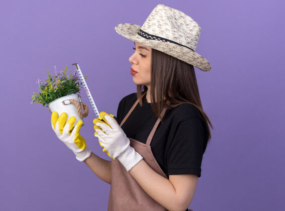 漂亮自信漂亮的白人女园丁戴着园艺帽和手套用卷尺量着紫色的花盆帽子手套园艺