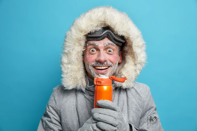 假期快乐的雪人喜欢极限运动在寒冷的霜天在山上穿着滑雪护目镜和夹克热饮有白色霜冻在脸上徒步登山积极休息的概念冬天外套烧瓶