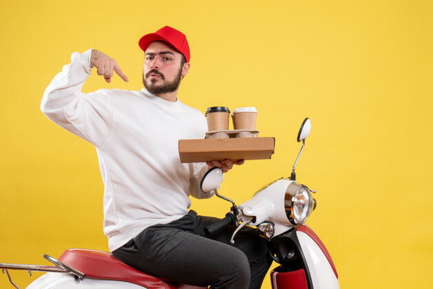人黄色墙壁上手持咖啡和食物的男性快递员的正视图食物持有头盔