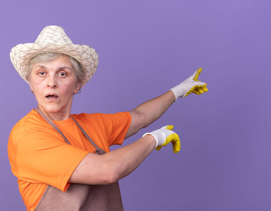 园艺自信的上了年纪的女园丁戴着园艺帽和手套指着紫色的侧面帽子信心女