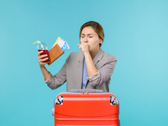 旅行前景度假中的女性拿着果汁和机票在蓝色背景上咳嗽旅行度假海上飞机举行航行女人