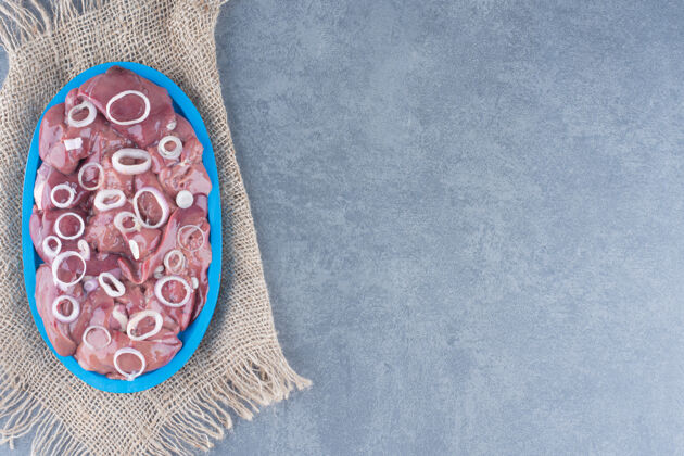 番茄生肉片和洋葱片放在蓝色盘子里烹饪柠檬粗麻布