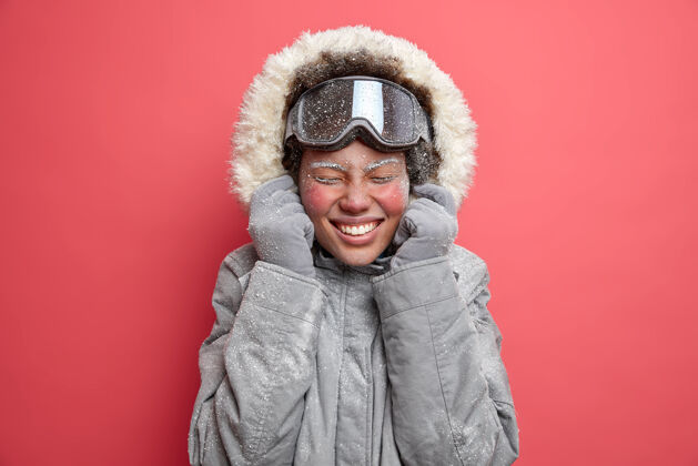 运动喜出望外的女人戴着灰色夹克兜帽笑容可掬满脸红霜的照片在十二月去滑雪季节请女人