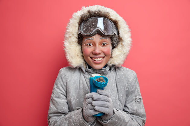 冰积极向上的女人在寒冷的天气里花时间在户外喝热水瓶里的热饮料 穿着外套高兴地微笑着霜冻冬天红色