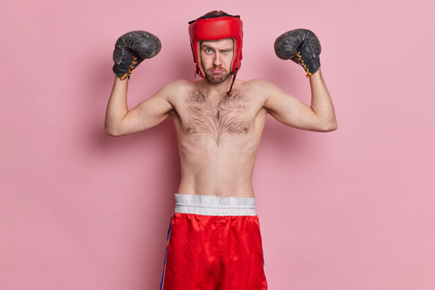 躯干积极的运动员喜欢拳击戴防护帽手套举起手臂展示肌肉有瘦的身体赤裸的躯干站着认真看男性严肃打架