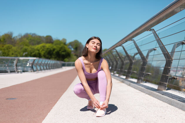 女人在炎热阳光明媚的早晨 年轻女子在桥上穿运动装系鞋带身体动机运动员