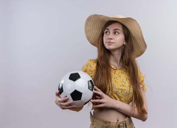 复制表情严肃的年轻女孩戴着帽子拿着足球看着左边的空白处和空白处年轻女孩球
